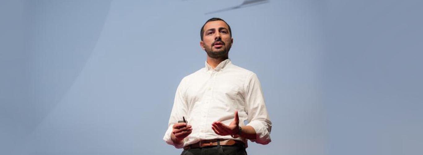 Image of Dr. Muneeb Ali wearing a white shirt in front of a large blue screen